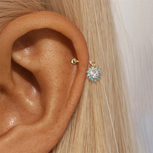 Detailopname van gouden S925 hart helix piercing met blauwe kralen en zirkoon op het oor