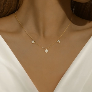 Macro view of dainty gold necklace featuring three clover pendants with cubic zirconia