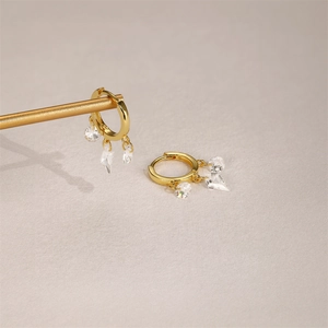 Detail of gold fan earrings with sparkling geometric crystal pendants on a textured surface