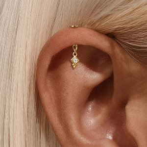 Nahaufnahme eines goldfarbenen Piercings mit geometrischem Zirkonanhänger am Ohr