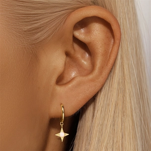 Detail of gold-plated silver hoop earring with star pendant and opal stone on model