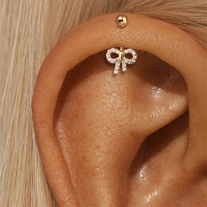 Gedetailleerde close-up van een gouden strik conch piercing met witte zirkoon op het oor