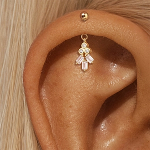Macro-opname van goudkleurige kraakbeenpiercing met geometrische hanger van zirkoon