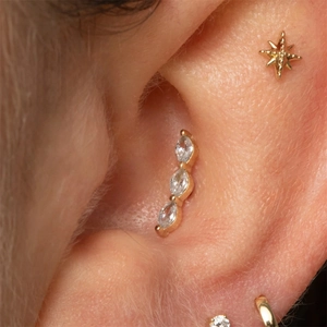 Détail macro du piercing conch doré avec trois zircons clairs de taille marquise