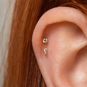 Gros plan sur un piercing en or avec trois cristaux de zircon alignés verticalement