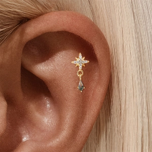 Detailed close-up of a gold North Star ear piercer with a blue gemstone drop on the ear