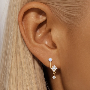 Macro view of gold flower earring featuring blue opal and clear zircon on model