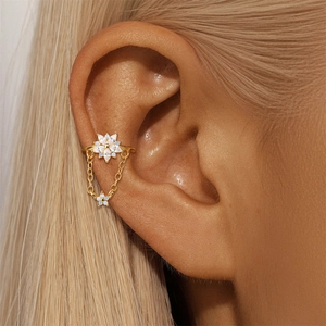 Vista macro di un earcuff a fiore dorato con zirconi marquise e catena pendente