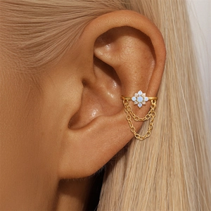 Dettaglio di ear cuff dorato con fiore di opale blu e nappine a catena pendenti