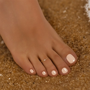Close-up of minimalist gold toe ring with single white zircon on sandy beach background