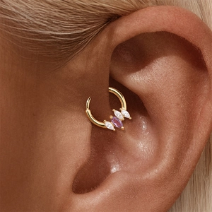 Close-up of golden daith piercing hoop with marquise-cut purple and white gemstones
