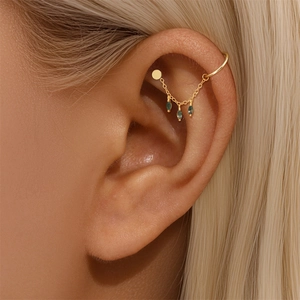 Close-up of golden tassel earrings with three green marquise gemstones on a model