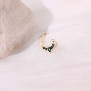 Detailed view of a gold clicker ring with five inlaid green gemstones on white fabric