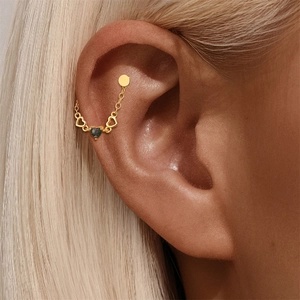 Makro-Detail des goldenen Knorpel-Piercings mit Herzmotiven, grünem Stein und Kette