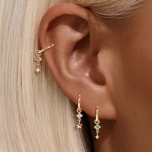 Dettaglio di orecchini a stella dorati con gemme rosa e verdi indossati sul lobo
