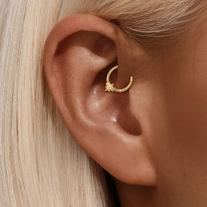 Close-up of a gold geometric starburst conch piercing worn on a model's ear