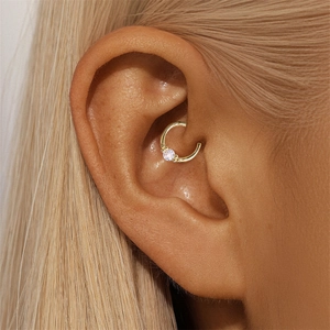 Macro detail of gold Daith piercing ring with a clear zircon stone on ear cartilage