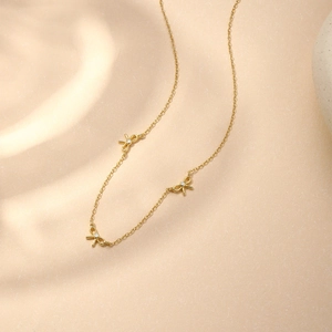 Détail du collier doré orné de trois pendentifs nœuds avec cristaux blancs incrustés