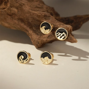Détail macro de boucles d'oreilles émaillées montagne et vague sur support en bois