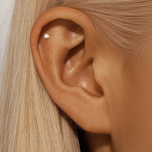 Macro shot of a minimalist S925 silver moissanite stud earring on the ear cartilage