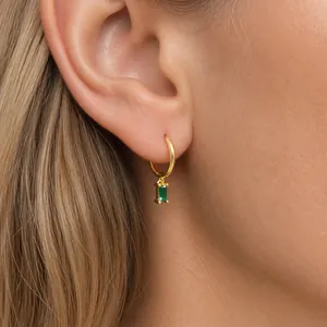 Detail of gold hoop earring with emerald green rectangular stone pendant on ear