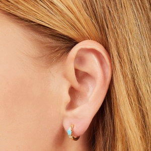 Detail van gouden oorring met druppelvormige turquoise steen en zirkonen op het model