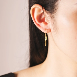 Primer plano de pendientes colgantes de oro de 18K con piedra verde en una modelo