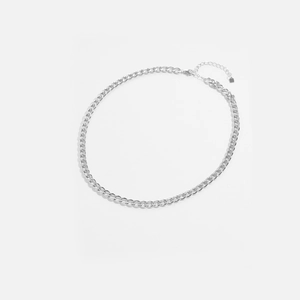Gros plan d'un collier chaîne gourmette argentée avec fermoir mousqueton et pendentif carré