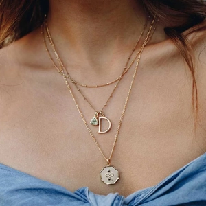 Close-up of a layered gold necklace set featuring green zircon and engraved pendants