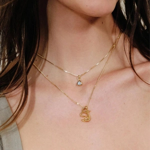 Layered gold necklaces featuring triangle pendant and gothic initial S pendant