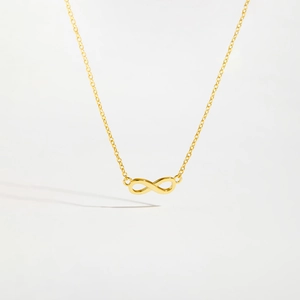 Polished gold infinity pendant on a delicate cross chain over a white background