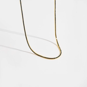 Détail d'un collier tennis doré avec des petites pierres de zircon bleu sur fond blanc