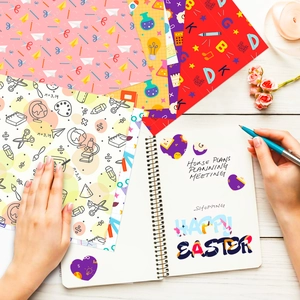 Hands decorating a planner with patterned craft paper on a white wooden table surface