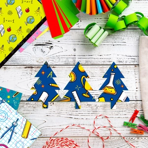 Close-up of tree-shaped paper cutouts with science motifs on a white wood surface