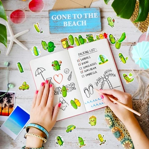 Close-up of cute cartoon cucumber stickers being applied to a notebook by hand