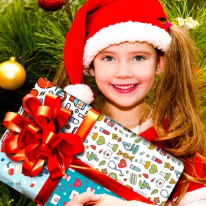 Niña sosteniendo regalo médico con lazo rojo frente a un árbol de Navidad decorado