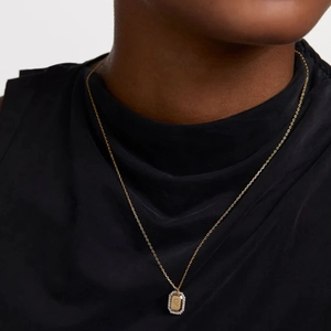 Close-up of a gold rectangle zodiac pendant necklace with white zircon pavé on a model