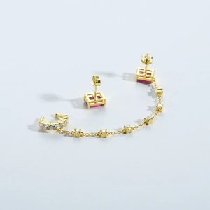 Détail de boucles d'oreilles dorées avec pierres rouges carrées et manchette à chaîne