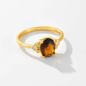 Vista macro de anillo dorado con gema ovalada marrón y detalles de diamantes laterales