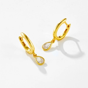 Macro detail of gold hoop earrings featuring elegant pear-cut clear zircon pendants