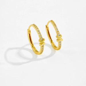 Detailansicht goldener Schleifenohrringe mit weißen Zirkonia auf weißem Hintergrund