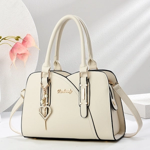 Sac bandoulière élégant blanc cassé avec breloque cœur et logo doré sur un socle minimal