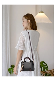 Detail of black structured crossbody bag with wine red handle and cute bear charm