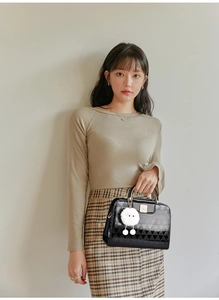 Detail of black glossy geometric handbag with gold handle and white plush charm accessory