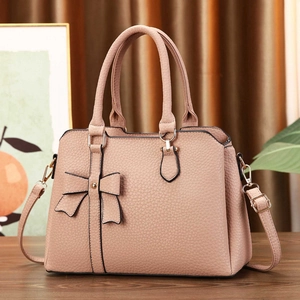 Nude pink bow handbag with litchi texture and golden hardware on a wooden table