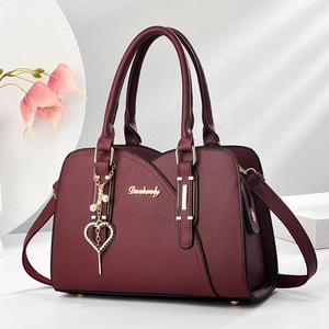 Elegante weinrote Leder-Handtasche mit goldenem Herzanhänger und verstellbarem Schultergurt