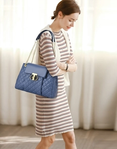 Close-up of quilted pattern blue leather bag with gold T-lock on striped dress