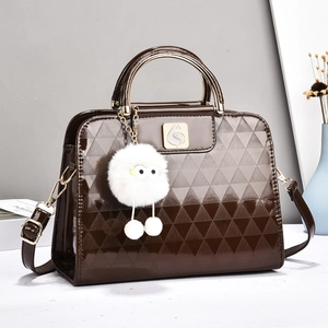 Detail of dark brown glossy patent handbag with geometric patterns and golden bird lock
