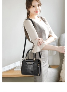 Detail of black crocodile texture handbag with gold logo and glossy leather finish