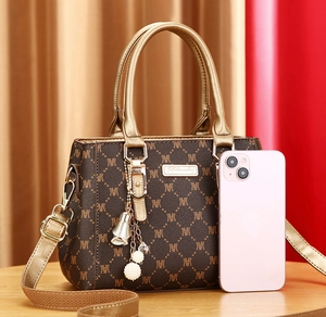Detail of vintage tote bag with gold ring handle, monogram pattern, and pearl charm